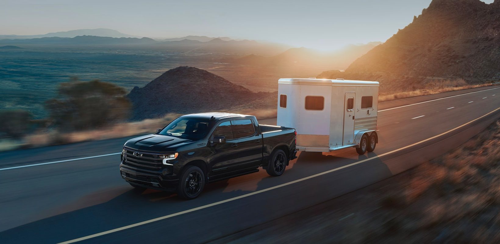 Chevrolet Silverado 1500 Crew Cab towing a two-horse trailer on a desert highway at sunset